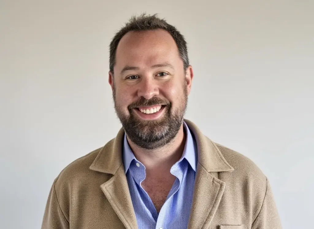 Dan Hardee smiling in a tan jacket and blue shirt